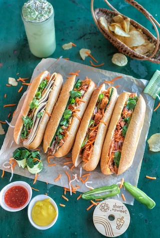 Four Vietnamese Banh Mi sandwiches with various fillings served on parchment paper.